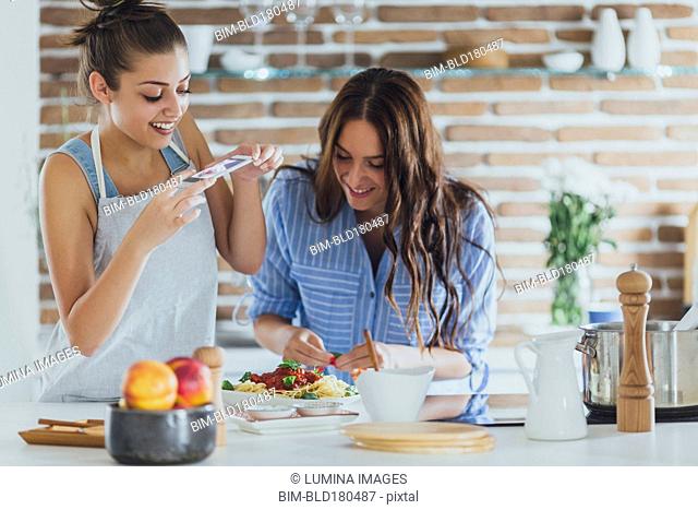 Caucasian women photographing pasta in kitchen