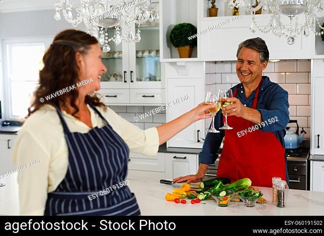 Happy senior caucasian couple in kitchen cooking together, drinking wine