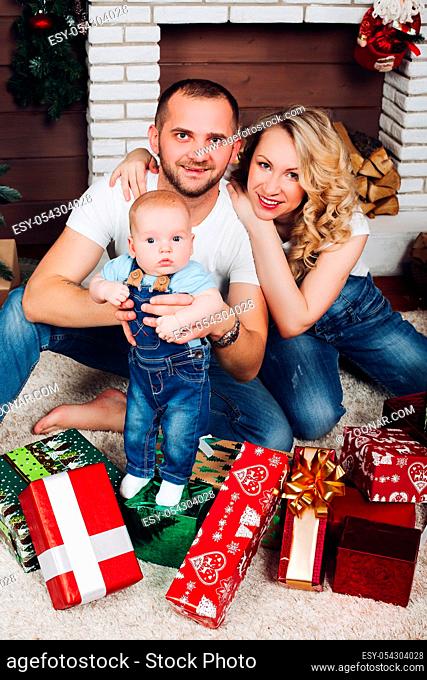 Positivity family posing together near fireplace and presents for Christmas and happy smiling at camera. Mom holding little son