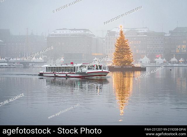 06 December 2023, Hamburg: The ship ""Alsterschwan"" sails past the illuminated Christmas tree in the middle of the Binnenalster