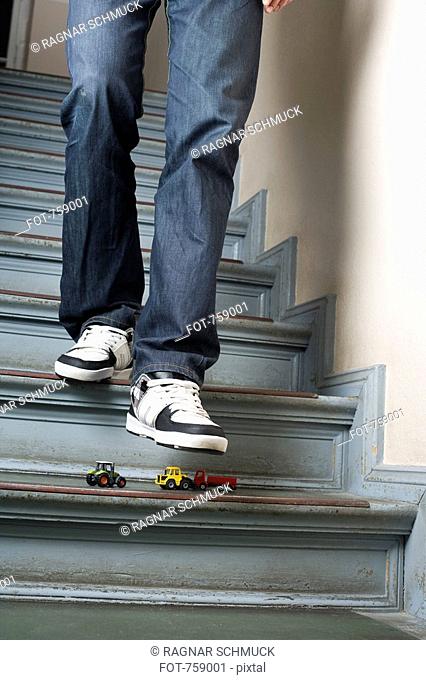 A man walking down stairs about to step on toy cars