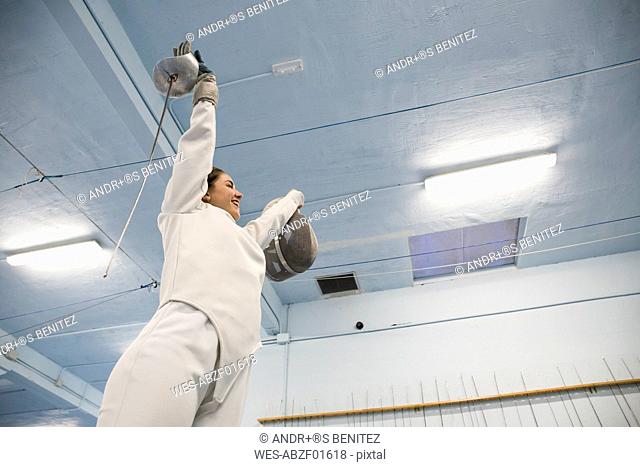Female fencer with arms raised celebrating her victory after a fencing match