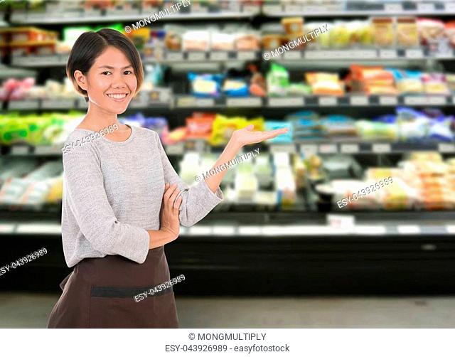 Smiling woman employee standing in supermarket shelf for your advertising