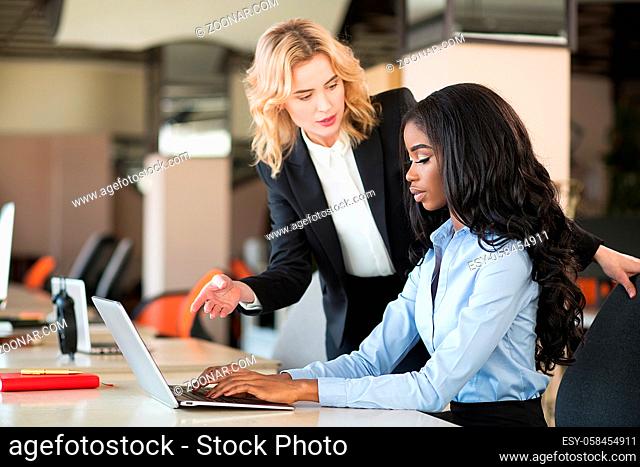 Africam american woman sitting at desk. er white colleague standing nearby