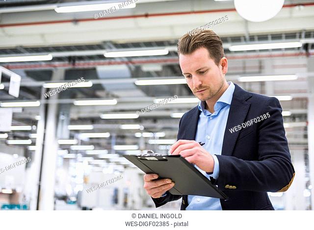 Man standing in factory shop floor taking notes