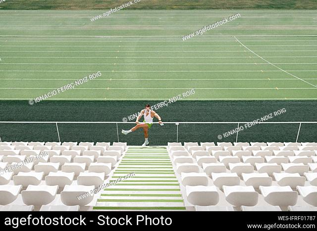 Sportsman doing warm up exercise on railing at stadium