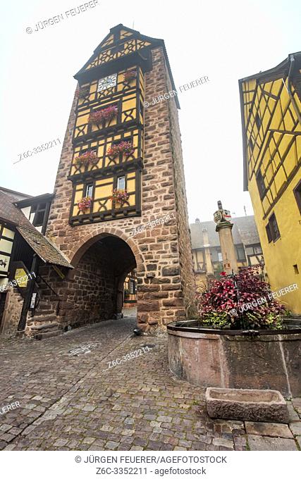 old town gate of the village Riquewihr with timberwork, Alsace Wine Route, France, the landmark Dolder tower and flower-bedecked well
