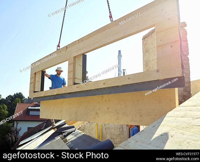 Workers installing wooden frame on top of house with crane machine