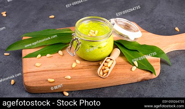 Pesto made from wild garlic, pine nuts and feta cheese in a glass, with fresh leaves on a dark textured background, empty space for text