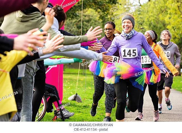 Enthusiastic female runners in tutus high-fiving spectators at charity run in park