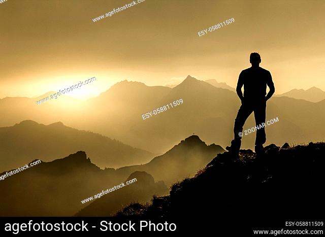 Relaxed man watching dreamfully towards sunrise and spectacular staggered mountain range silhouettes with bright back light