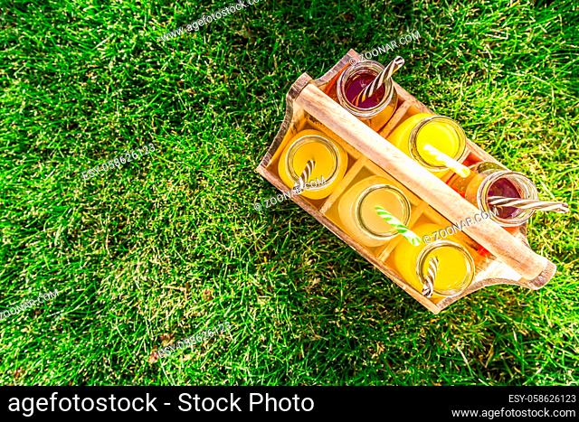 Assortment of lemonade and ice tea in bottles in wooden rack in the grass