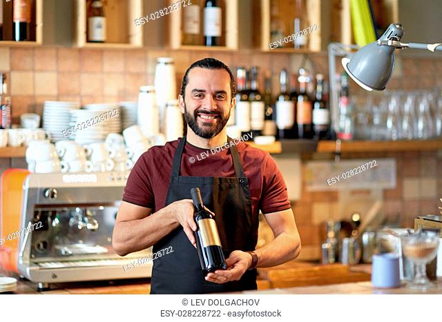 small business, alcohol drinks, people and service concept - happy man or waiter with bottle of red wine at bar