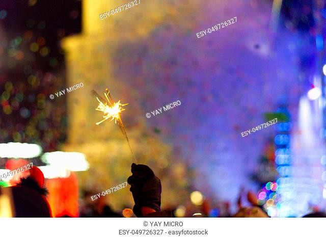 New Year celebration on main square. A lot of smoke or fog, lights, salute and confetti. Blurred colorful background. Bengali fire in hand with glove on...