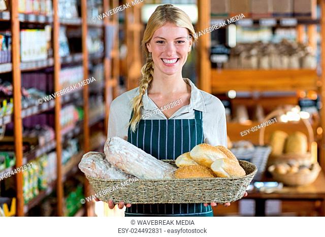Smiling female staff holding basket of bread at bread counter