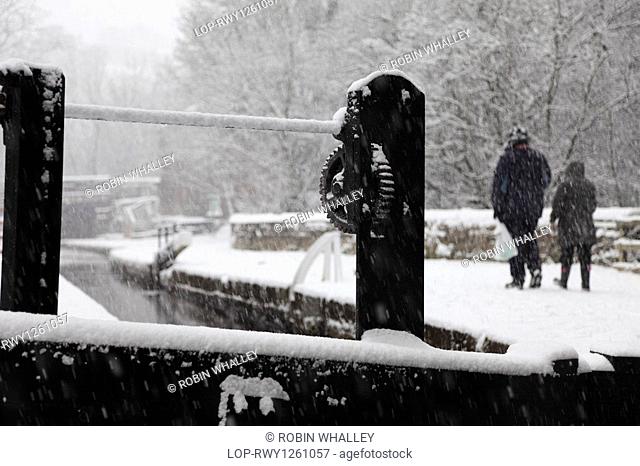 England, Lancashire, Saddleworth, Two people walking along a towpath by the Huddersfield Narrow Canal in the snow