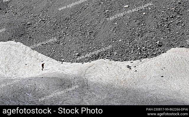 dpatop - PRODUCTION - 11 August 2023, Bavaria, Ramsau: A hiker walks over the remnants of snow on the Watzmann Glacier. Researchers give them only a few more...
