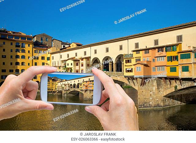 In the bottom left of the photo are hands holding smart phone and taking picture of Ponte Vecchio in Florence (Tuscany, Italy)