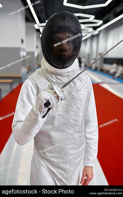 Portrait of teenage boy fencer wearing uniform posing with sword for camera. Swordsmanship and fencing martial art concept