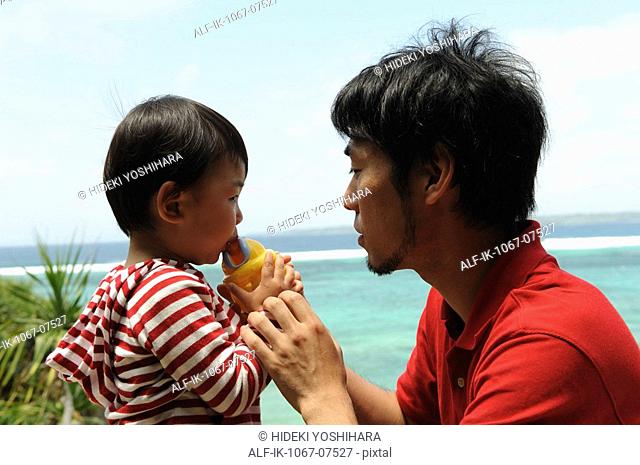 Child drinking water with his father on beach