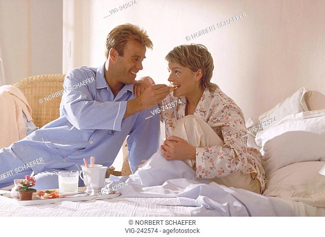 portrait, indoor, half-figure, young blond couple wearing pyjama sit on a Sunday morning at breakfast in bed  - GERMANY, 07/03/2005