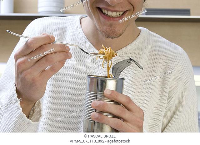 Close-up of a young man eating noodles from a can with a fork