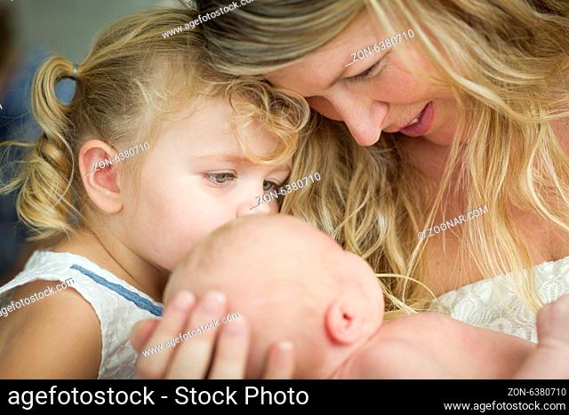 Beautiful Young Mother Holds Newborn Baby Girl as Young Sister Looks On