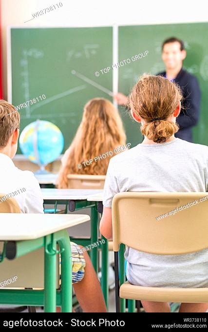 Teacher or educator or docent standing while lesson in front of a blackboard and educate or teach students or pupils or mates in a school or class