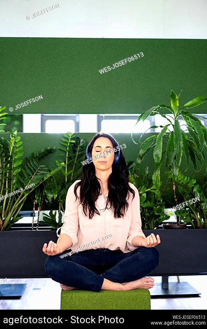 Businesswoman with headphones meditating in coworking office