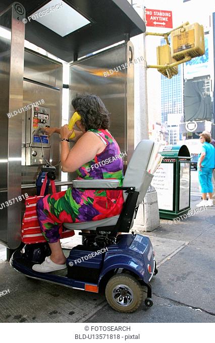 Woman with a disability, utilizing a scooter for mobility, using a public pay telephone