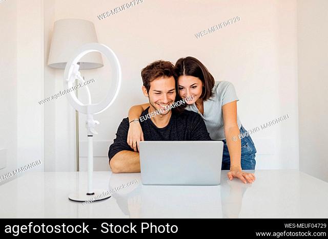 Smiling young couple using laptop together on table at home