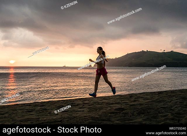 Fit young woman with a healthy lifestyle smiling while running on the beach during summer vacation in a cloudy day in Flores Island