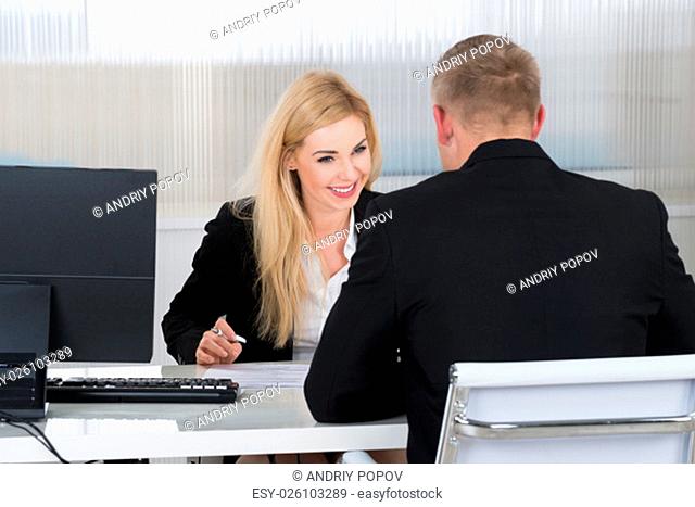 Smiling young businesswoman interviewing male candidate at desk in office