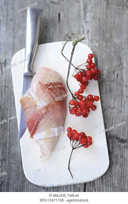 Raw chicken breast wrapped in bacon next to a sprig of guelder rose berries