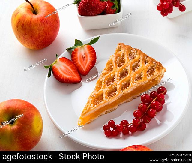 apple pie slice on white plate with currant and strawberries