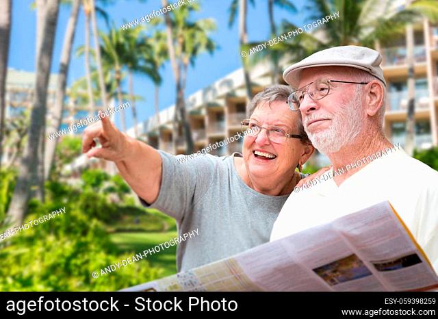 Happy Senior Adult Couple Tourists with Brochure Next To Tropical Hotel and Palm Trees