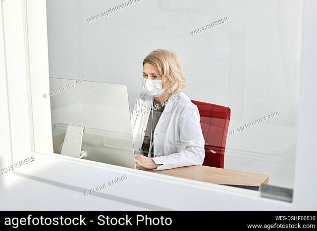 Radiologist using desktop PC in clinic seen through window