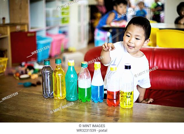 Young boy playing with a selection of bottles with colourful liquids in a Japanese preschool