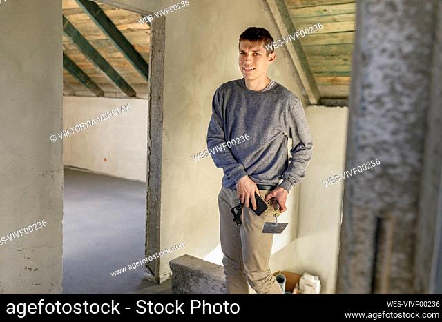 Smiling young man holding trowel and smart phone at home