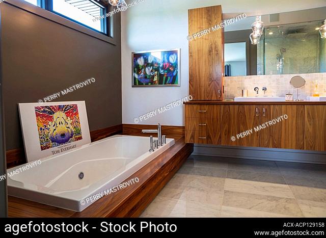 Walnut wood vanity and base with deep white acrylic bathtub in en suite with grey and white nuanced marble floor inside a luxurious modern cube style house