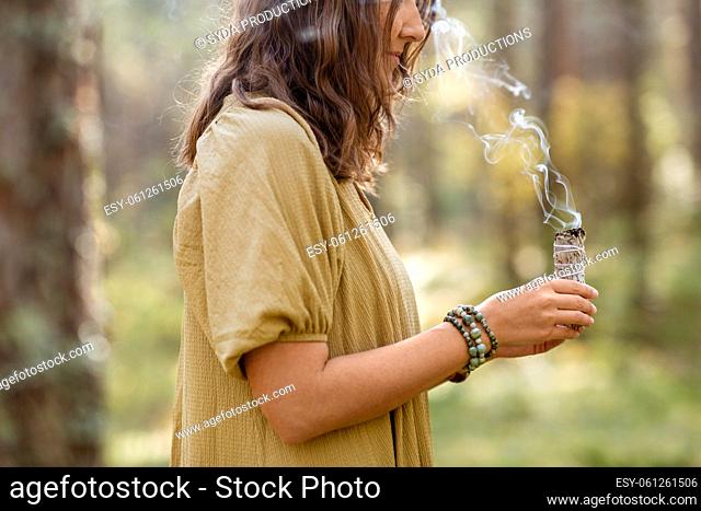 woman with sage performing magic ritual in forest