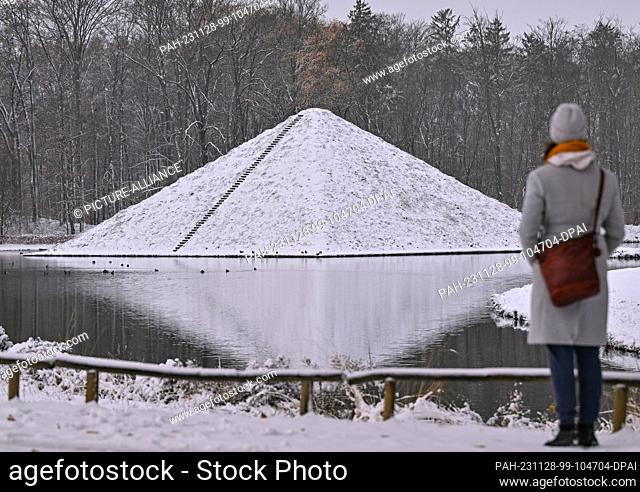 28 November 2023, Brandenburg, Cottbus: A woman stands in front of the snow-covered lake pyramid in Prince Pückler Park in Branitz