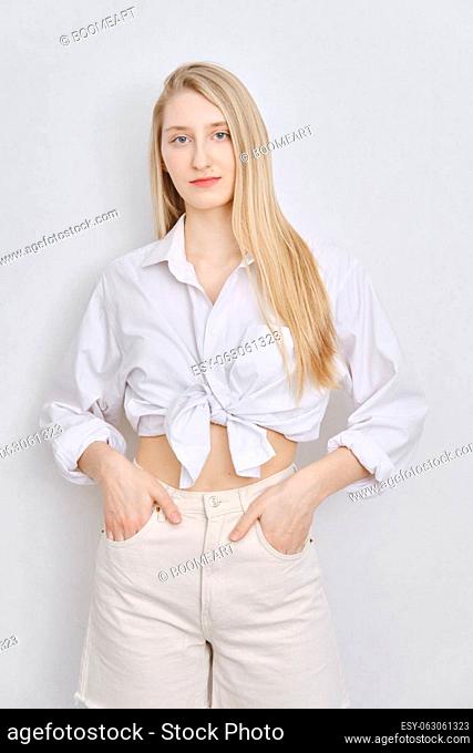 Casual portrait of young woman in white shirt and shorts standing over white wall