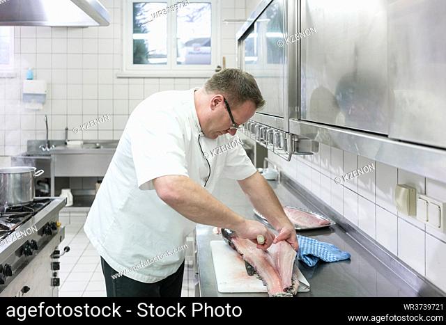 Chef in restaurant or hotel kitchen filleting carp fish
