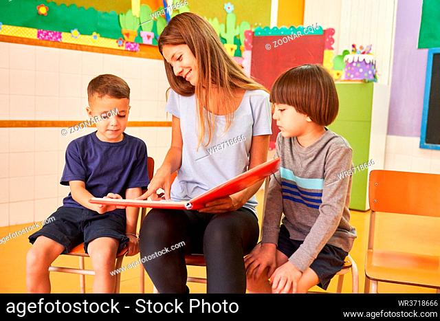 Kindergärtnerin und zwei Kinder beim Buch vorlesen in der Kindertagesstätte oder Vorschule