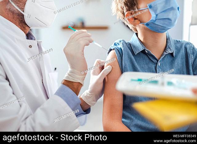 Doctor with protective face mask injecting vaccine to boy at center