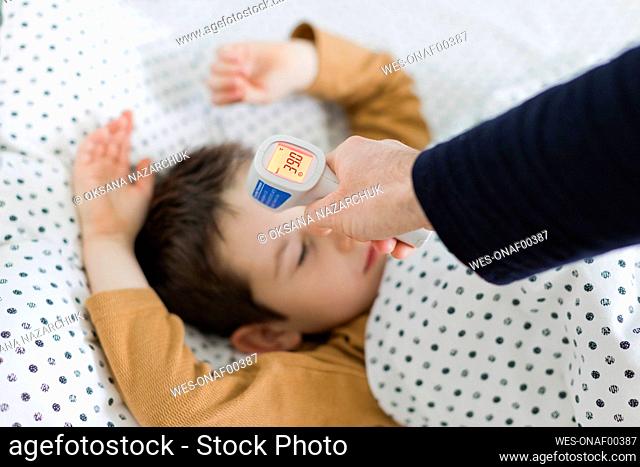Hand of father measuring temperature of son lying on bed at home