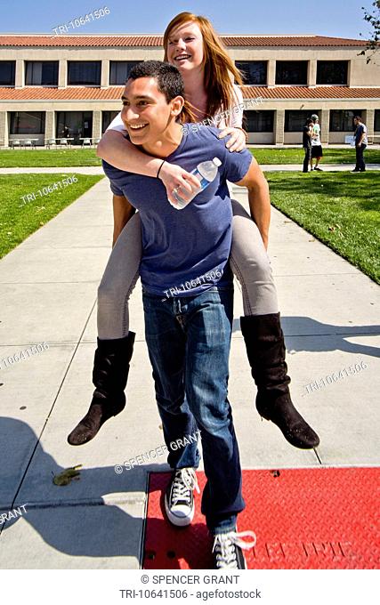 A Hispanic student carries his Caucasian girlfriend piggyback across the campus of Saddleback College in Mission Viejo, CA