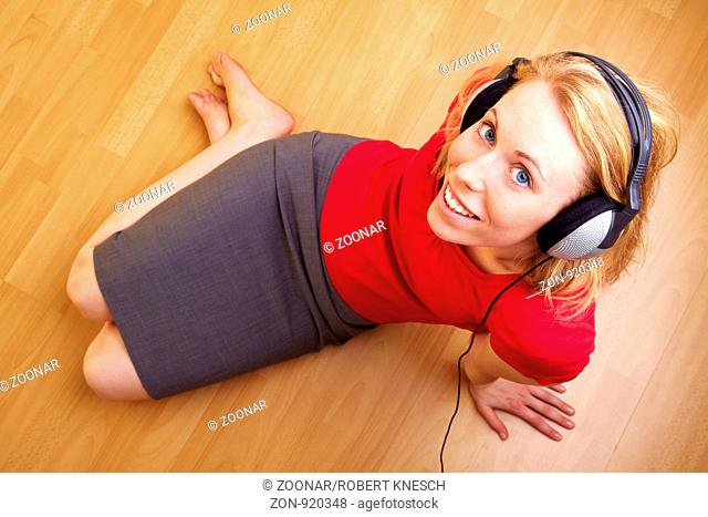 Blonde Frau sitzt auf dem Boden und hört Musik