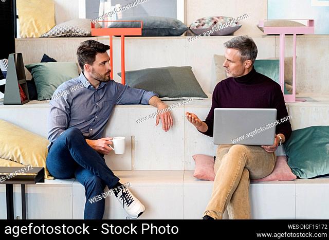 Mature businessman with laptop discussing with male colleague at office